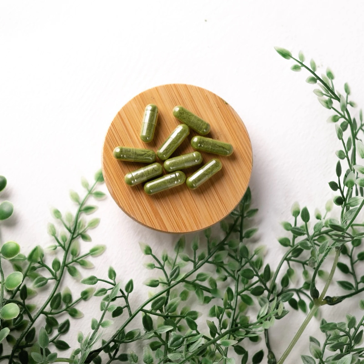 Green herbal capsules on a bamboo dish surrounded by fresh greenery