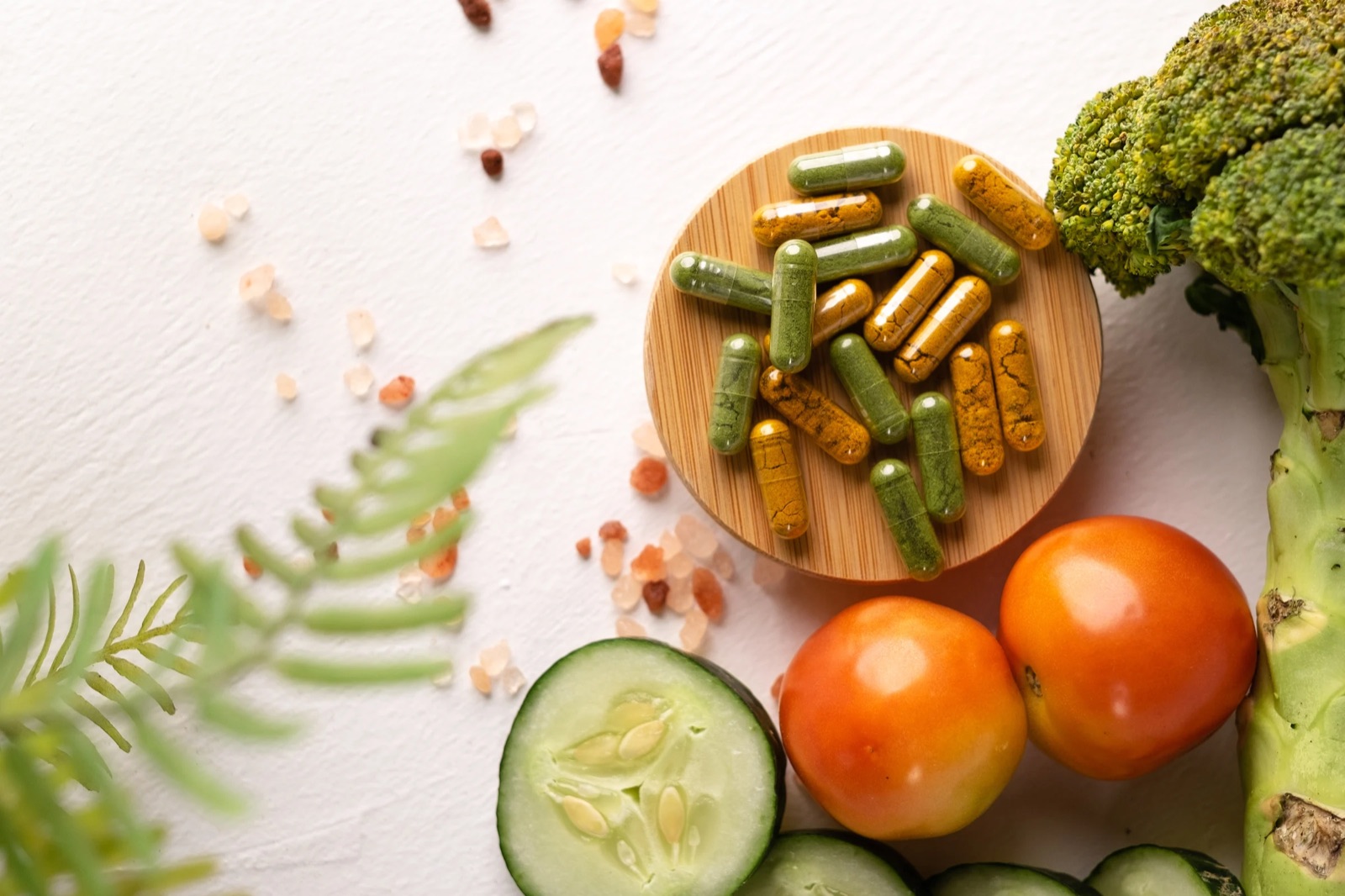 Herbal capsules on a bamboo dish beside fresh vegetables